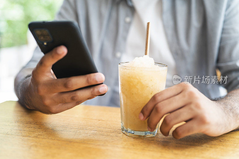 拉丁男子拿着智能手机喝冷饮