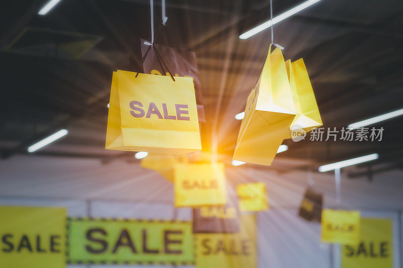 商店的天花板上挂着写有SALE字样的黄色购物纸袋。销售折扣的概念。