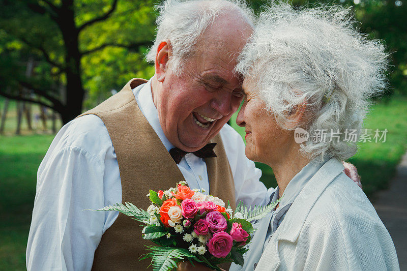 一对老夫妇在绿色的公园里散步。祖母和祖父在金婚纪念日庆典上。奶奶和爷爷笑着拥抱着。50年的浪漫爱情故事。