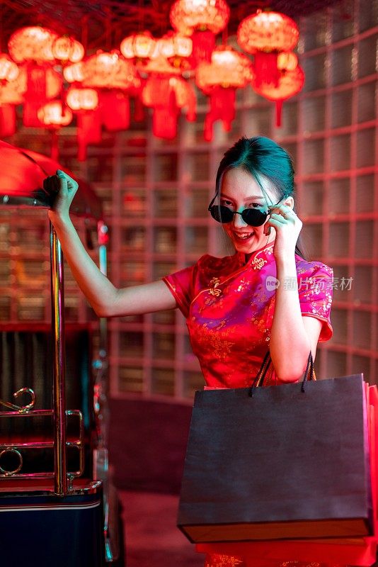 一位年轻的亚洲女模特肖像照片，戴着太阳镜，穿着红色中国传统旗袍，在霓虹灯前看起来很酷，拿着购物袋在一辆嘟嘟出租车旁边