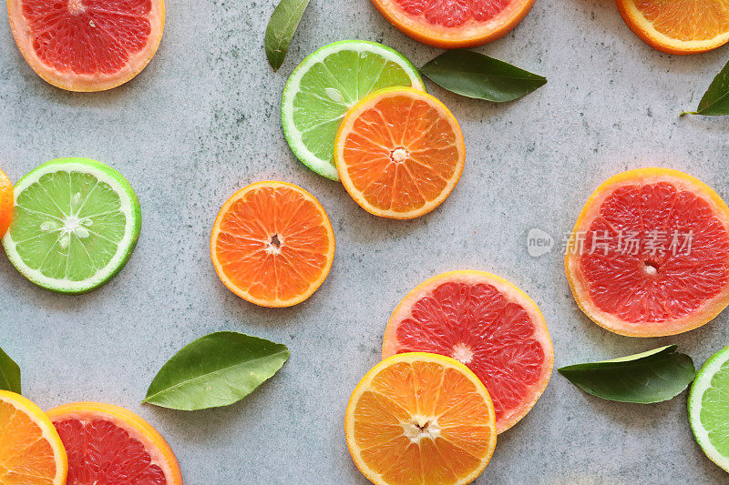 全帧图像柑橘水果切片的叶子，横截面的血橙，塞维利亚橙，柠檬和酸橙，斑驳的灰色背景，提高的观点