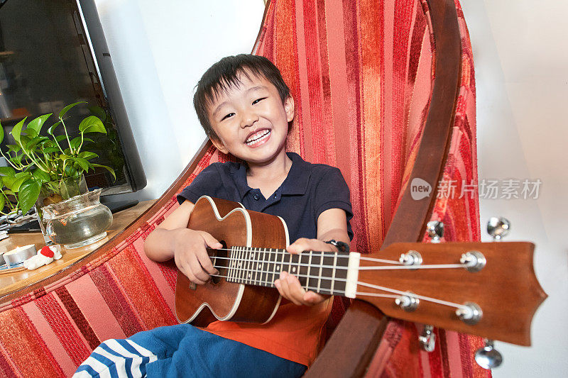 小男孩坐在红沙发上弹吉他