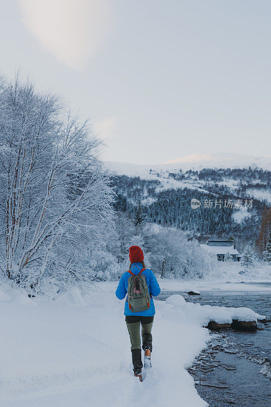在挪威日落时分，一个背着背包的女人走在风景秀丽的冬季湖泊山景的后视图