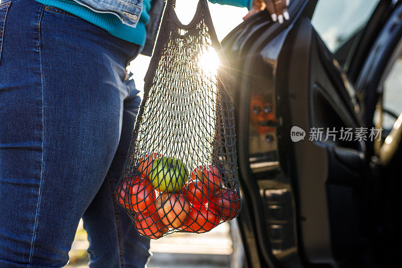 年轻女子打开车门，装载可重复使用的网袋苹果里面