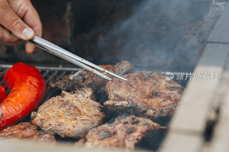 男人在烤架上烤肉，用烹饪镊子把肉翻过来