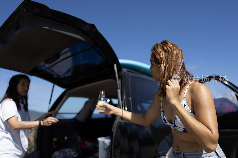 一名亚裔华人妇女在海滩停车场递给她的朋友椰子油