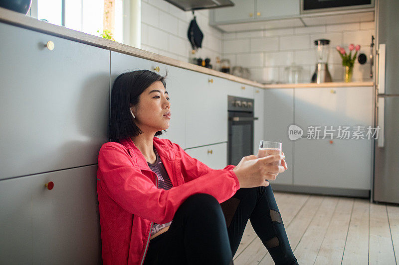 年轻的成年女性在锻炼后在厨房喝着一杯水