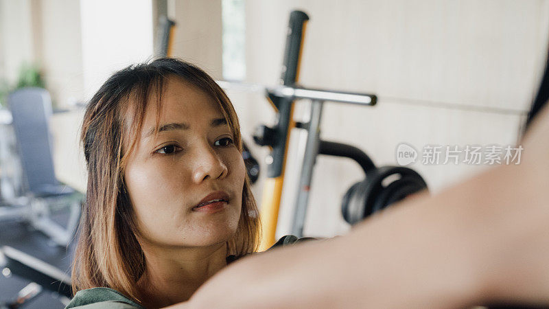 近景:年轻的亚洲体育运动女性在现代健身房里积极训练，健美运动员拉下钢索。