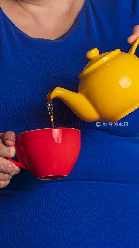一个女人把茶从黄茶壶倒到红杯子里的特写。