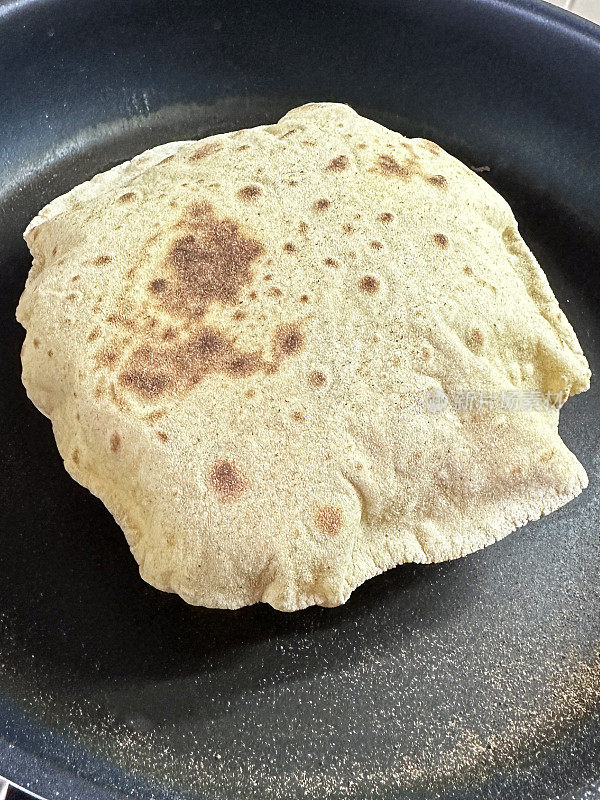 不粘锅的全画幅图像包含膨胀的roti，用全麦atta面粉制成的chapatti，在厨房灶台上烹饪，高架视图，重点在前景