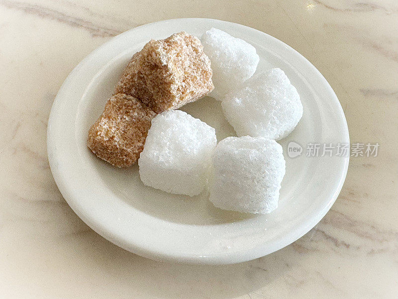 美味的红糖和白糖块放在一个白色的小碟子上