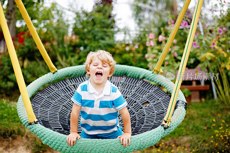 有趣快乐的学龄前男孩在户外操场上玩链式秋千。快乐的微笑的孩子在温暖的夏日里玩耍和荡秋千。与孩子一起积极休闲