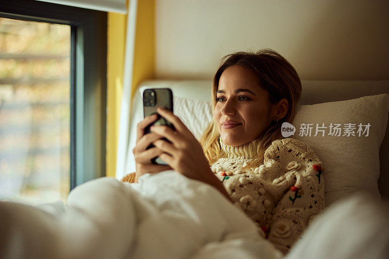 一个微笑的女孩，在家里休息，用手机，刷社交媒体。