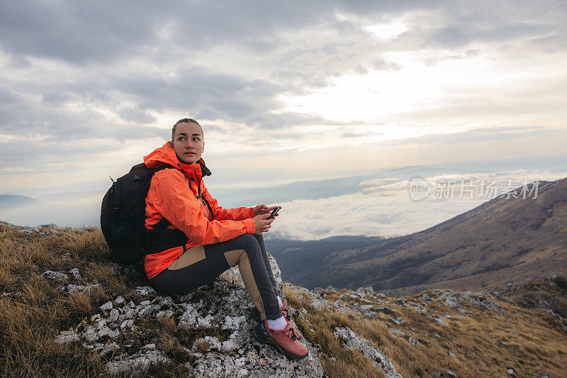 美丽的女徒步旅行者坐在山顶的岩石上