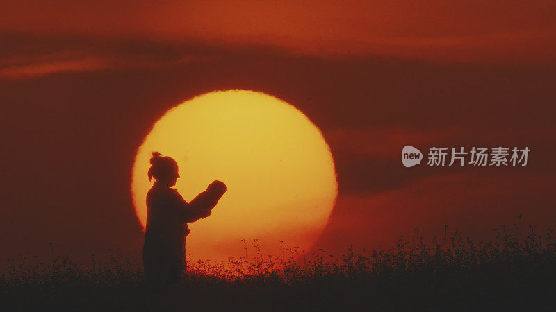 夕阳下，母亲抱着婴儿，背景是橙色的天空