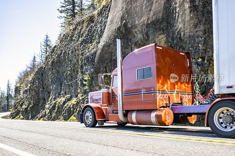 加长驾驶室橙色大钻机经典半挂车运输货物在干货车半挂车行驶在山路与岩石和树木