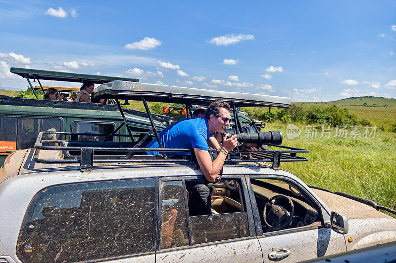 一名游客在肯尼亚的游猎旅行中拍摄野生动物。一名男子在一辆敞篷游猎车上带着相机在非洲旅行。马赛马拉国家公园，肯尼亚。