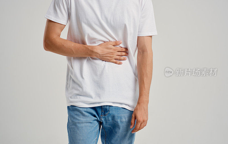 穿着白色t恤和牛仔裤的男子用手摸着他的胃胃疼消化不良