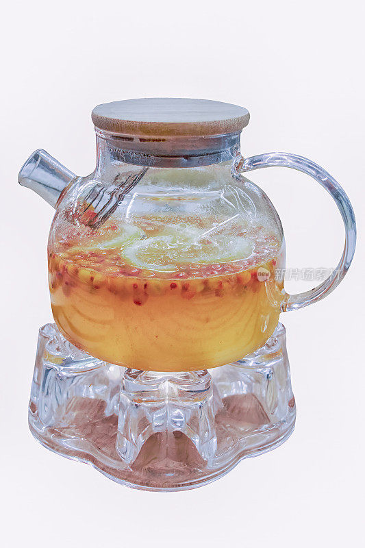 玻璃茶壶与水果柠檬沙棘茶在温暖的支架孤立在白色背景。