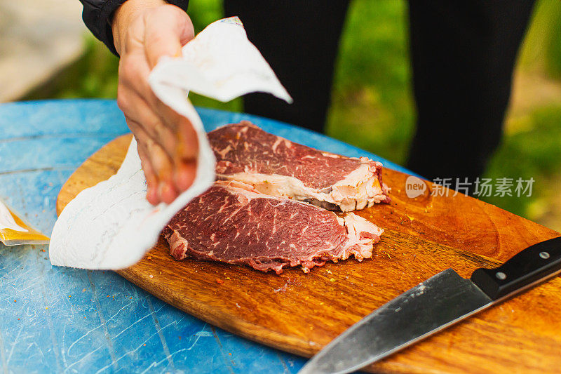 新鲜牛排。满足户外经验。晚餐在后院。木板上红肉。准备食物的过程。小牛肉。美味的小吃。户外用餐。盐和调味食品