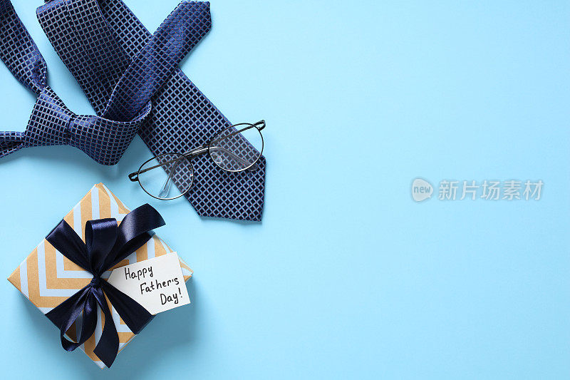 祝您父亲节快乐。淡蓝色的桌子上平放着“父亲节快乐”礼品盒、领带、眼镜。