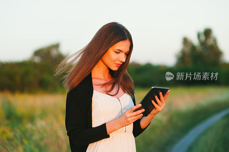 一个留着长发的年轻女子在日落的田野里用数码平板电脑