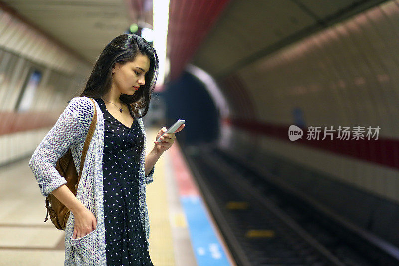 年轻女人看电话，乘客在车站等地铁，旅游女人在城市旅行