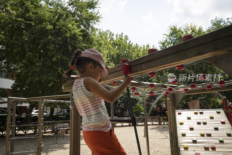 小女孩在操场上玩耍，沿着单杠吊着走