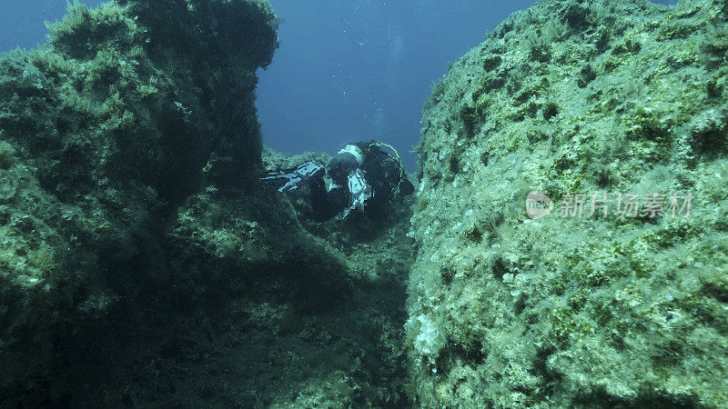 戴着水肺的潜水员游过岩石的裂缝。海底构造板块上的裂缝。海底板块的提坦式位移。地中海、塞浦路斯