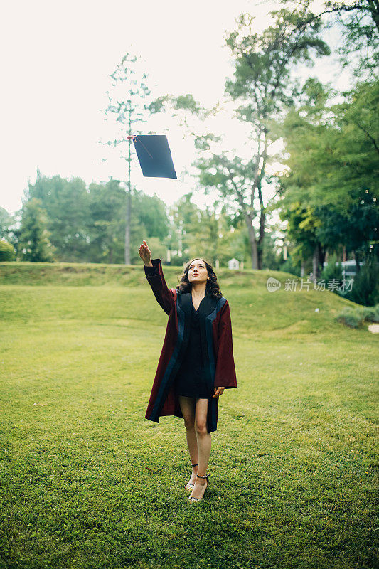 年轻女子穿着毕业礼服，将她的帽子抛向空中
