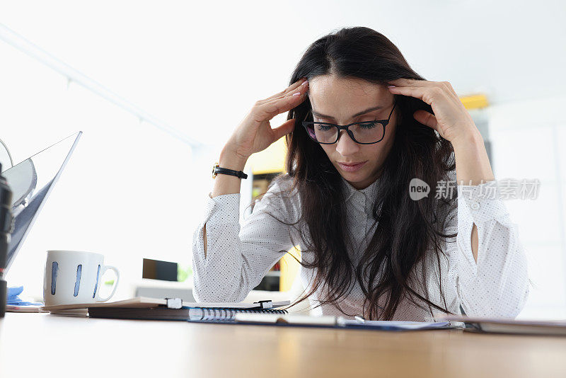 疲惫困倦的女人坐在桌子旁，在工作场所抱着头休息