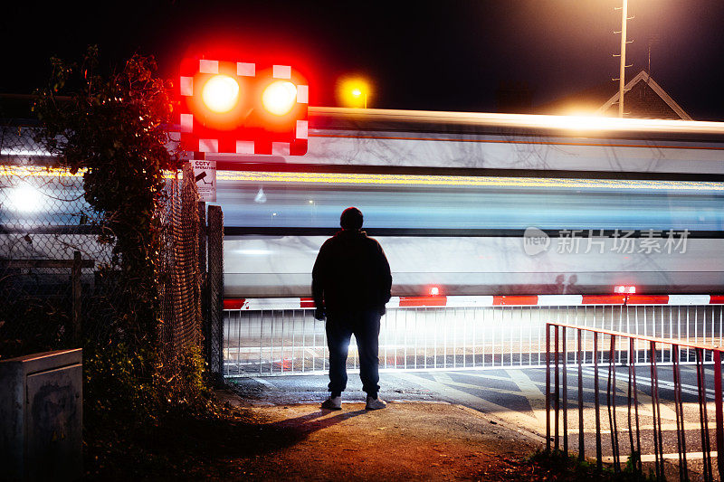 男子在铁路十字路口等待在夜间与模糊的运动，高速列车
