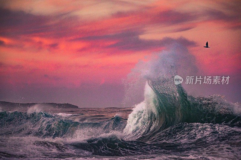 海浪碰撞着戏剧性的粉红色和红色的天空