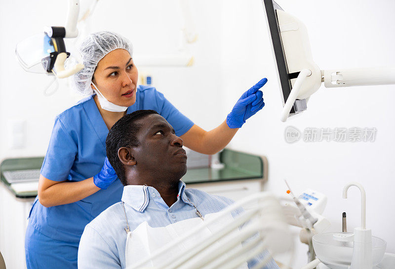 男人坐在牙科椅上，女牙医指着展品