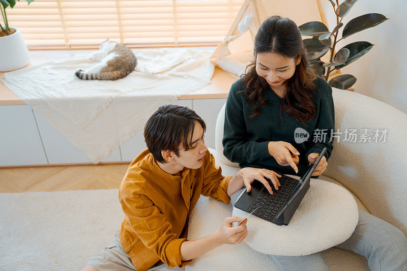 年轻的亚洲夫妇拿着平板电脑，在家接收包裹，享受送货上门服务。网上购物，移动支付。愉快的购物体验