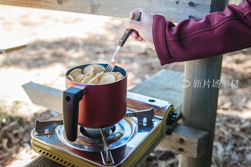 无法辨认的女人的手在乡下用野营炉做意大利饺子。