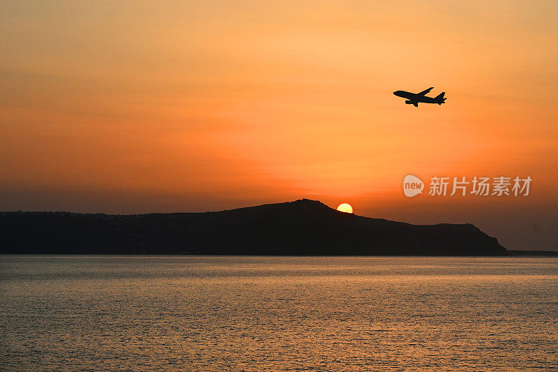 日落时分，度假飞机飞过希腊圣托里尼岛的火山口