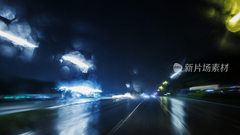 雨夜驾驶，灯光模糊:在暴风雨后的暴雨中航行。散焦光尾和镜头光晕