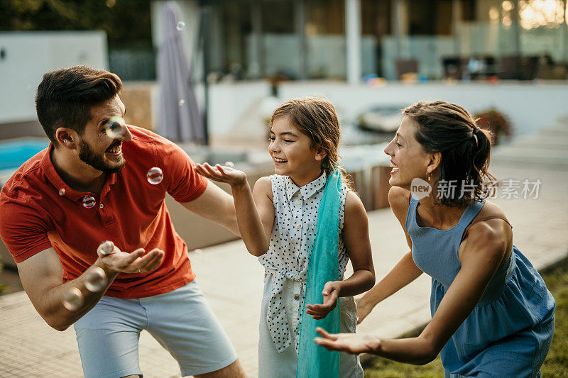 这是一张美丽的全家福，父亲、母亲和他们的小女儿，在他们舒适的郊区房子前享受一个有趣的下午，分享欢笑和乐趣