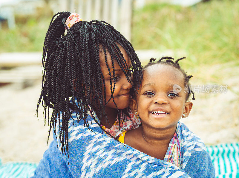可爱的年轻非裔美国儿童的肖像，姐妹，家人裹在沙滩毯子里