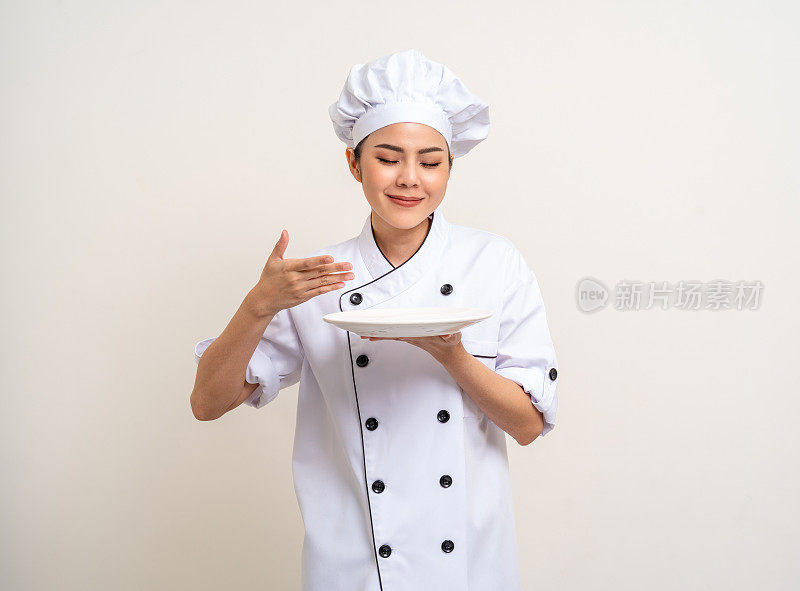 闻闻食物。漂亮的亚洲女厨师穿着制服，拿着盘子、勺子、器具在厨房里烹饪，各种姿势的菜单好好吃就孤立了。厨师女厨师人在厨房餐厅