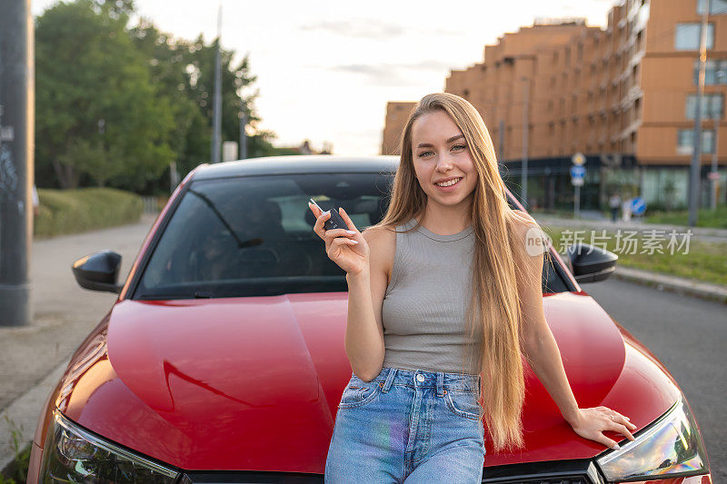 一位年轻的女司机自豪地把车钥匙拿在她闪亮的红色汽车前