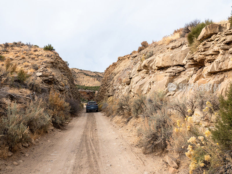 小型SUV在砂岩悬崖间狭窄的土路上行驶。