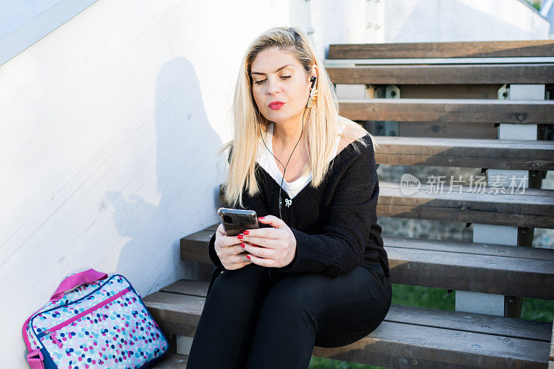 一个美丽的女商人的肖像，下班后在楼梯上享受户外，听音乐。商务人士带着电子设备上下班。