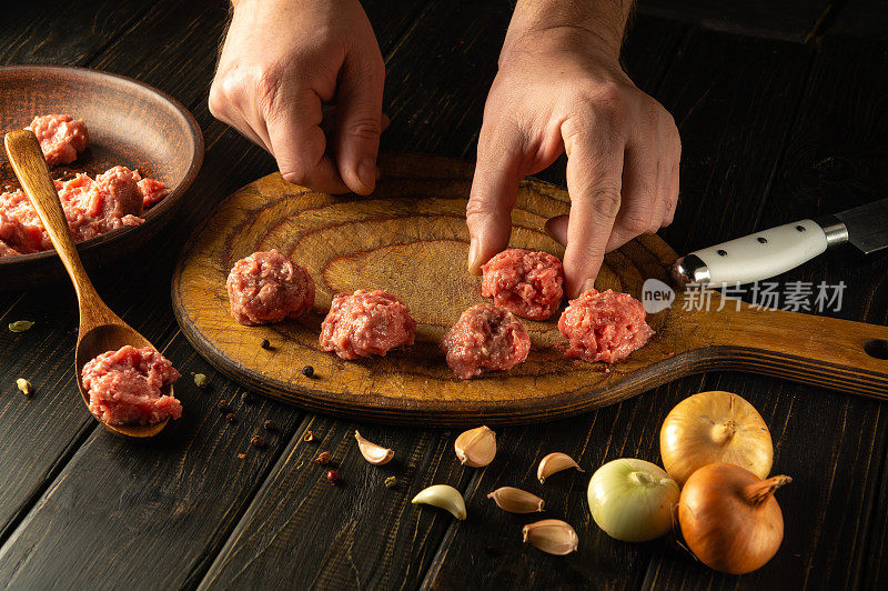 一个男人的手把一个肉丸放在厨房的板上。在厨房的桌子上煮肉。烹饪，食谱和营养的概念