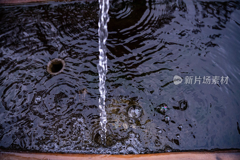 特写镜头:一股水流从天然泉水流入牛槽的木槽。水和气泡的运动