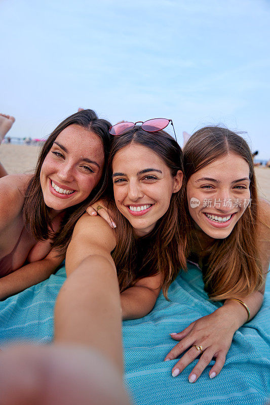 三位女性朋友躺在沙滩浴巾上，开心地看着镜头。
