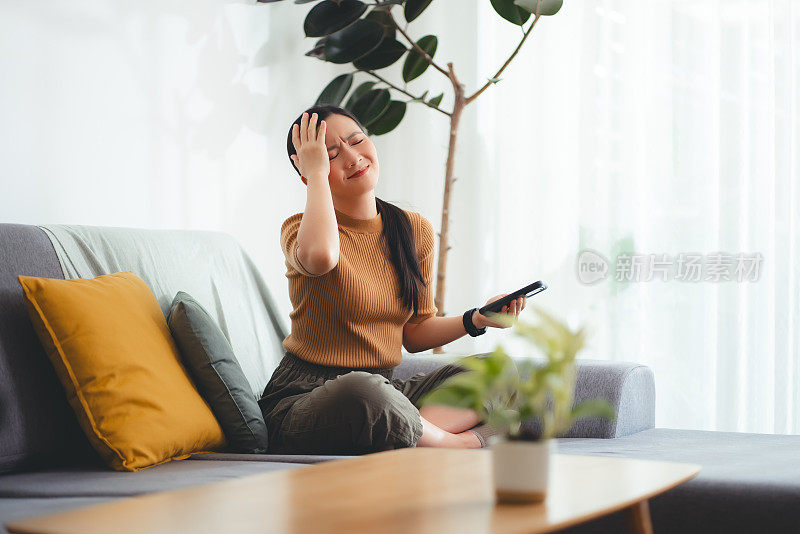 亚洲女性坐在家里看智能手机屏幕，有问题。