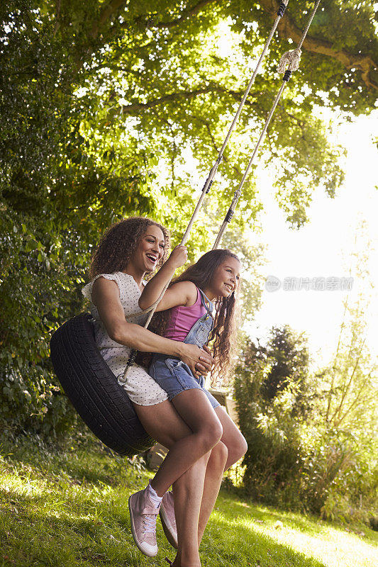 妈妈和女儿坐在花园里的秋千上