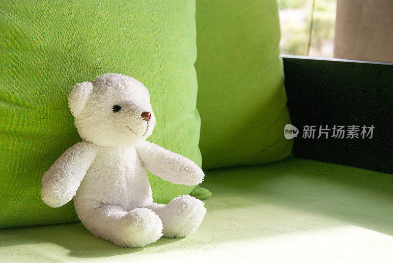 微笑的白色泰迪熊坐在沙发上，躺在绿色的枕头上